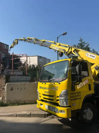 Şehir içinde bir binanın çatısına malzeme kaldıran kamyon üstü vinç